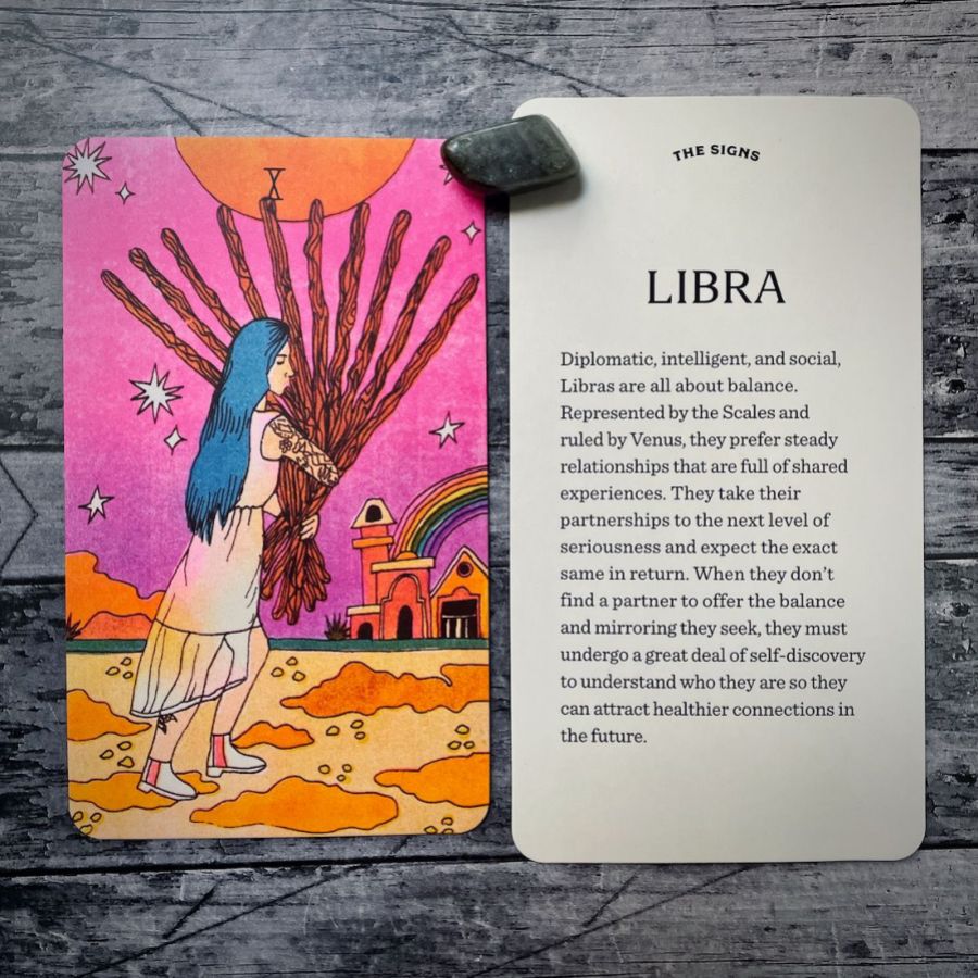 In two tarot cards on a grey background:  Left: A woman with blue hair down her back is holding 10 wooden sticks as she crosses an orange terrain and in front of a pink sky. There is a rainbow over the houses in the background. Right: Libra