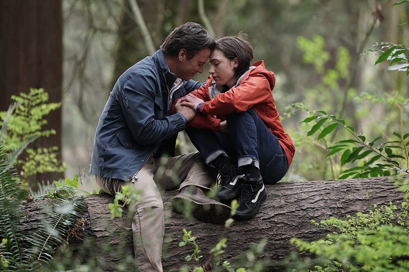Clark and Maddox embrace, while sitting on a log in the forest.