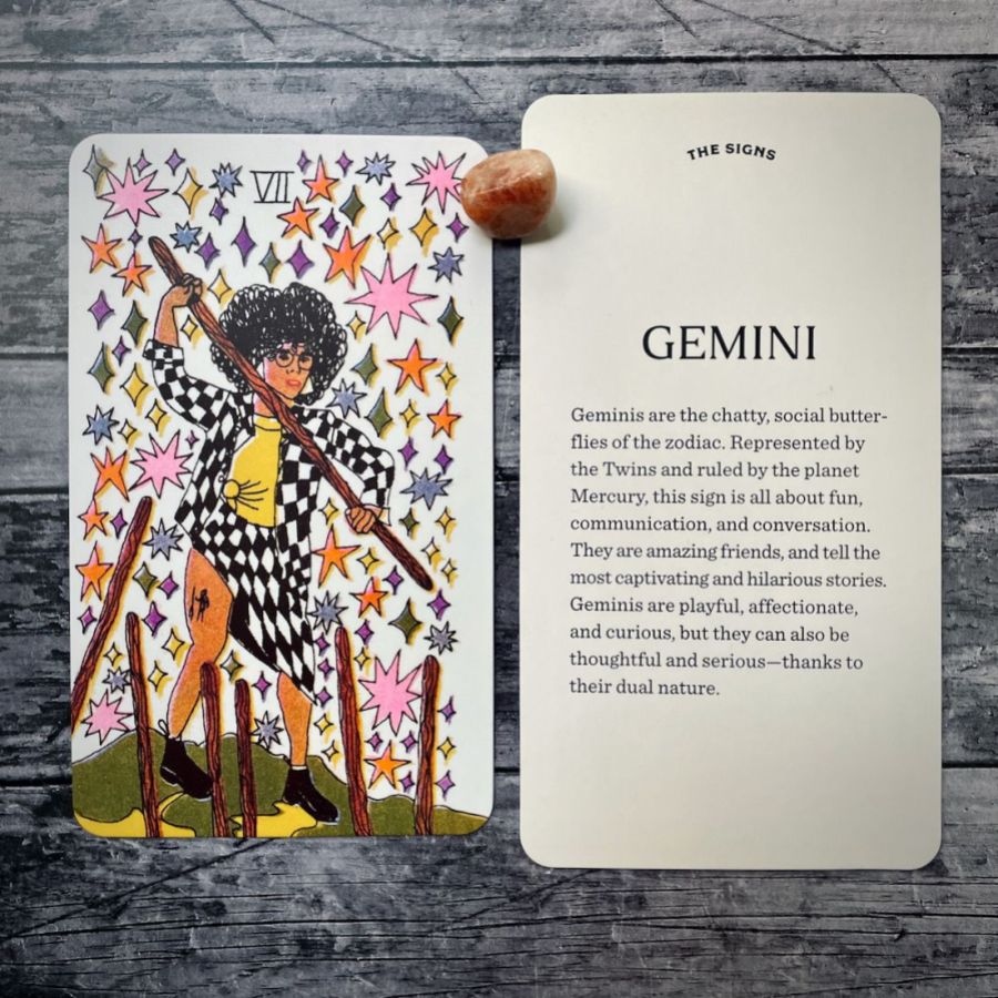 In two tarot cards on a grey background:  Left: A black woman with an afro and glasses is wearing a black and white checkered coat and matching skirt, exposing her thigh tattoo. She has on a yellow shirt. There are multi-colored stars behind her as she digs into the ground with stakes. Right: Gemini