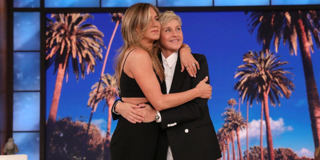 Ellen Degeneres and Jennifer Aniston hold each other in a hug on the last episode of the Ellen DeGeneres show. Jennifer Aniston is in a sleeveless black dress and Ellen is in a black blazer with a white button down.
