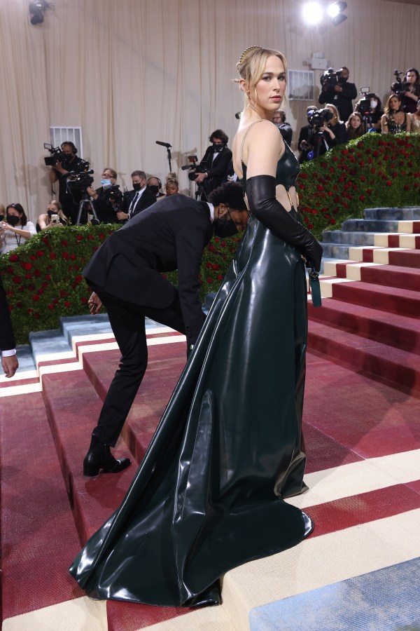 Tommy Dorfman in a dark green long latex gown and latex opera sleeves, her hair is pulled up away from her face, on the red carpet