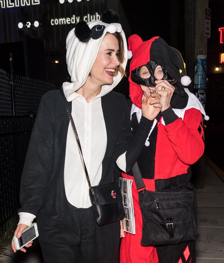 Sarah Paulson is wearing a panda costume, and Holland Taylor is wearing a jester costume. They are arriving at a Halloween party.