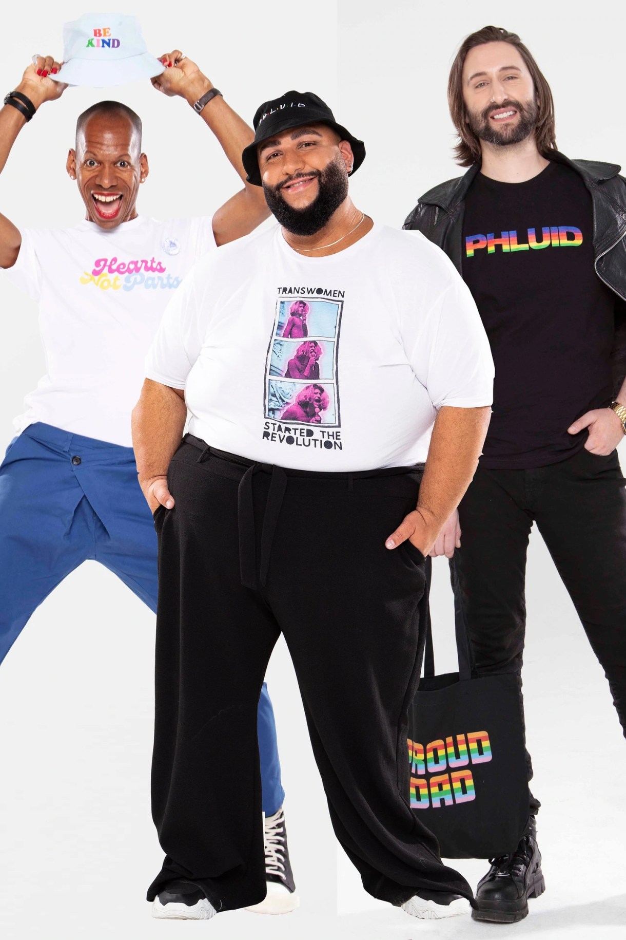 Three models in Phulid Project gear: hearts Not parts tee, "Trans Women Started the Revolution" and "PHLUID" in rainbow block lettering. The middle model is also holding a "PROUD DAD" tote bag.