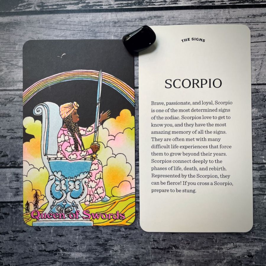 In two tarot cards on a grey background:  Left: A black woman with long braids and a head wrap sits on a blue thrown in yellow clouds in front of a rainbow on a night sky. She is in a dress of pink and clouds. She is holding a sword. Right: Scorpio
