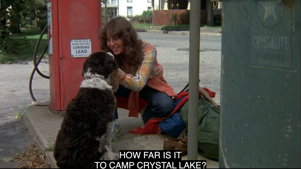 A white teenage girl holds a dog by the ears and says "how far is it to Camp Crystal Lake" in Friday the 13th
