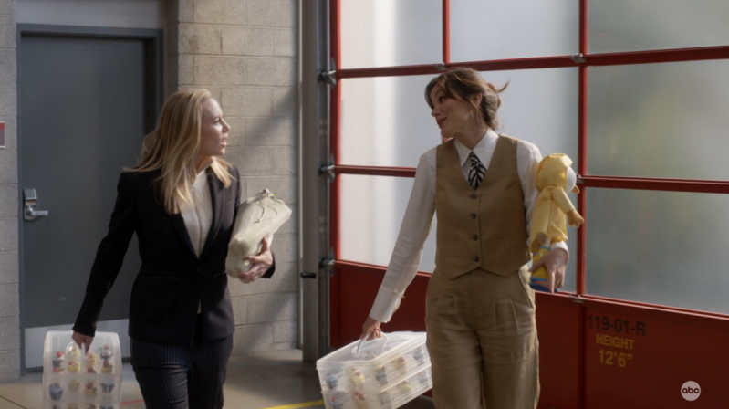 Maya and Carina are walking together in the firehouse on Station 19. The sun is creeping through the windows, Maya is in a half-zip pull over sweater underneath a blazer, Carina is in a tailored tan vest and suit pants with a tie and her hair in a bun.