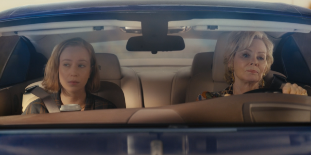 Ava and Deborah sit side-by-side in a car with Deborah in the driver's seat in the Hacks season two premiere.