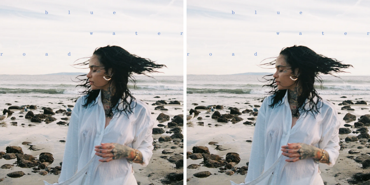 The album cover for Kehlani's "blue water road" features Kehlani on a stone-lined beach wearing a white buttondown, and their hair is blowing in the wind.