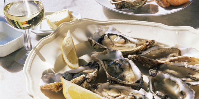 A plate of oysters and lemon slices sits next to a glass of white wine