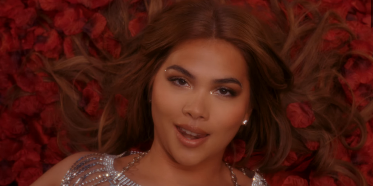 Hayley Kiyoko is wearing sparkles and laying in a bed of roses, singing into the camera in the For The Girls music video