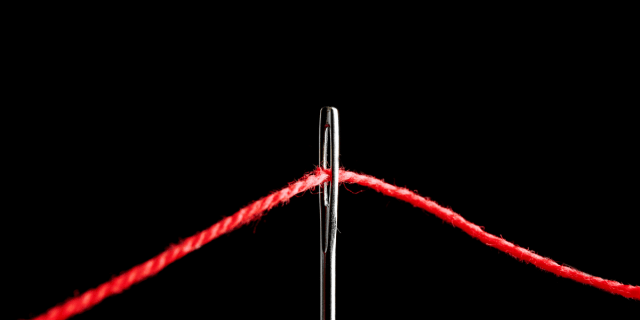 The top of a silver needle is visible against a black background. A red thread runs through it.