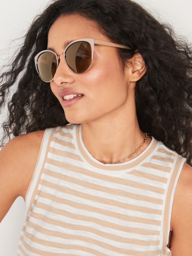 A light skinned brown woman in a striped tan tank top and long curly hair wears thin pink wireframe cat eye sunglasses with brown lenses