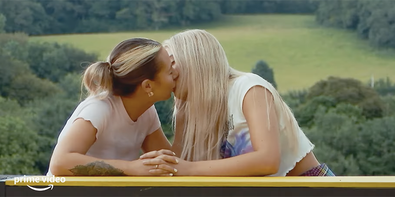 Two women kiss in front of a green field in Lovestruck High