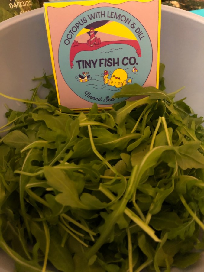 A large blue bowl holds arugula and a tin of Tiny Fish Co's octopus in lemon and dill