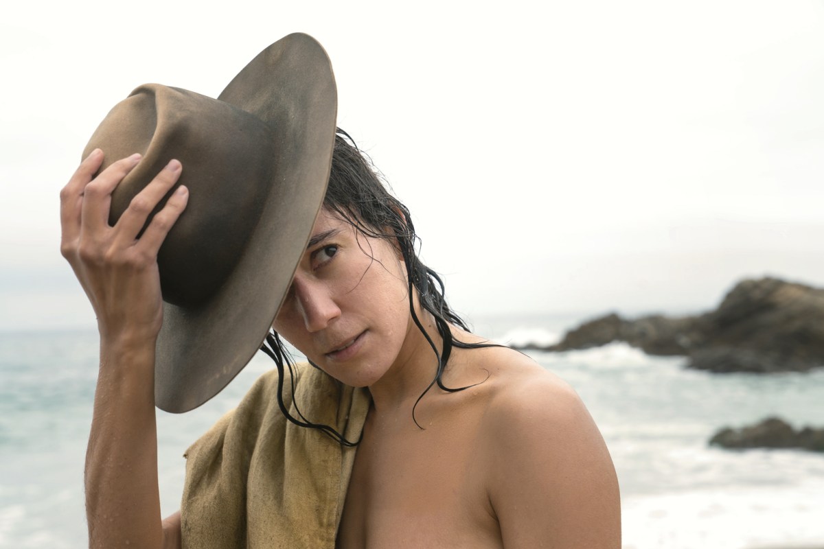 In Our Flag Means Death, Vico Ortiz takes off their hat while standing shirtless in front of the ocean