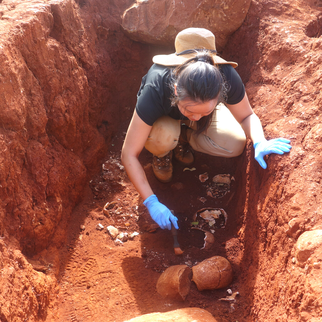 Viv in 2016 as a baby gay with long hair. She is in a grave brushing dirt off of a skull.