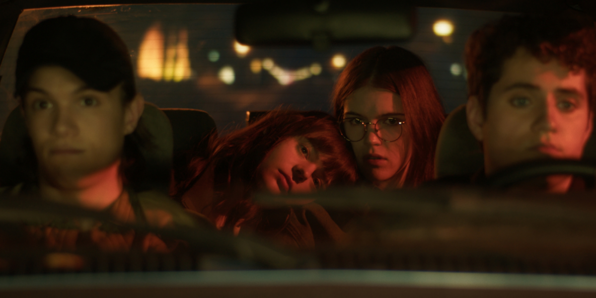 A girl rests her head on another girls shoulder in the back of a car.