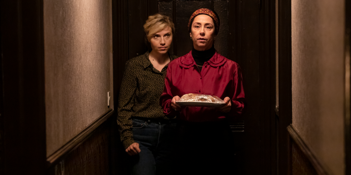 2 women stand in a dark hallway while they ominously look forward