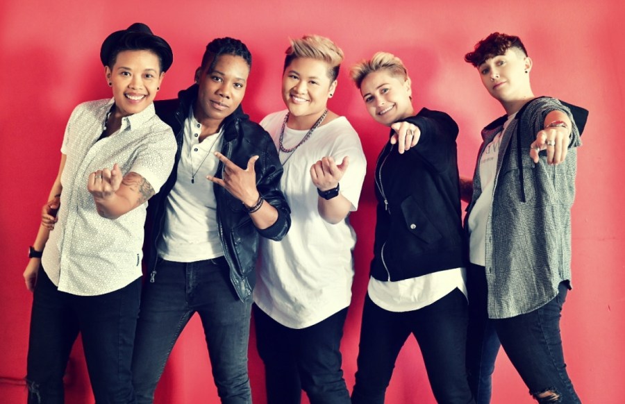 Five masculine of center folks wearing shades of white, black and grey against a red wall