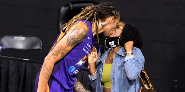 Cherelle Griner and Brittney Griner kiss after a WNBA basketball game. Cherelle Griner is in a green tank top and denim jacket, Brittney is in her Phoenix Mercury uniform.