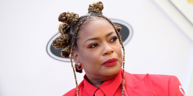 Aunjanue Ellis walks the red carpet for Essence's Black Women in Hollywood. Her hair is braided into bantu knots and her red suit coat is custom bedazzled with the word "Queer" spelled in crystals. Underneath the red suit coat is also a red button down.