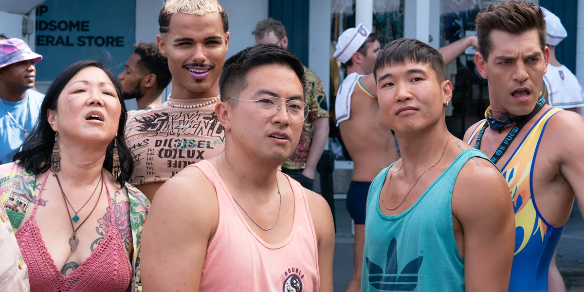 Margaret Cho stars in Fire Island, here she is in a red knit crop top showing off her tattoos while standing with her castmates (all of whom are gay men, also dressed for summer) on a boardwalk on Fire Island.