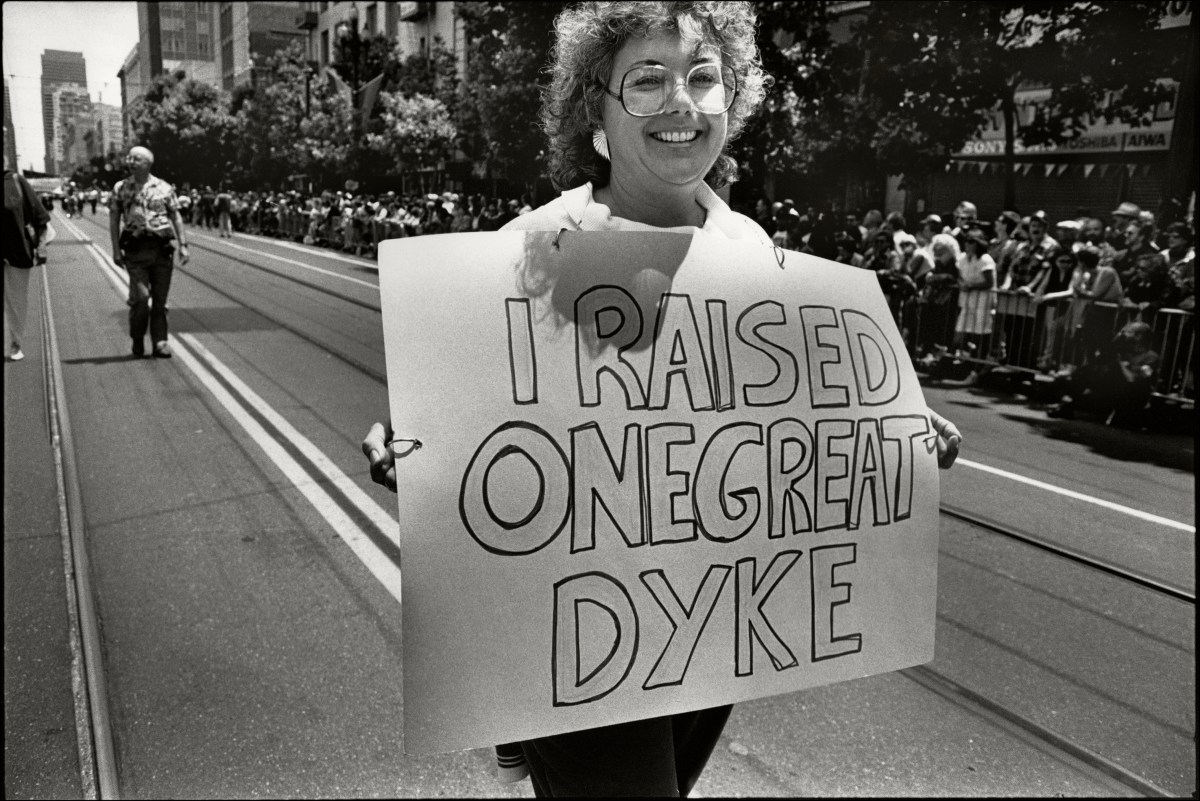 A woman smiles as she carries a sign that reads 'I Raised One Great Dyke'