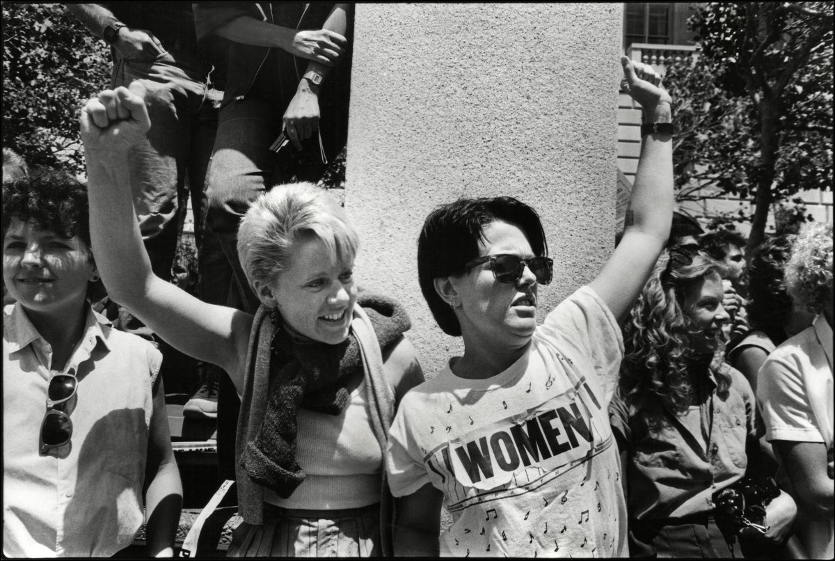 Two women raise their fists as they watch marchers during the International Lesbian & Gay Freedom Day Parade
