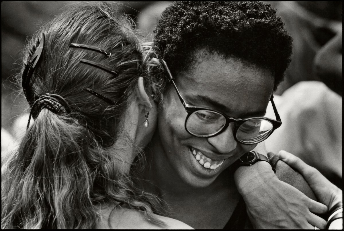 Close-up of a couple as they embrace, one woman is black with large glasses and she is smiling.