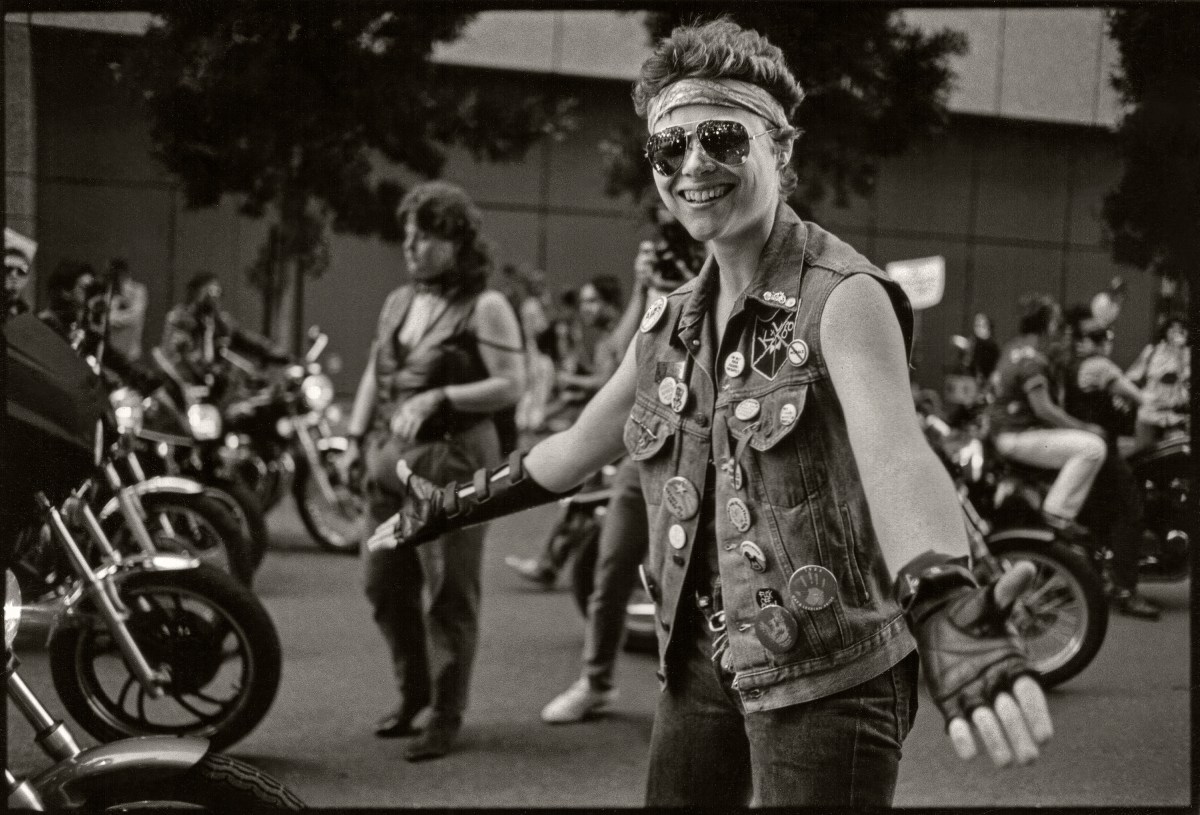 Portrait of smiling woman, dressed in a sleeveless denim jacket and fingerless gloves, from the 'Dykes on Bikes' 