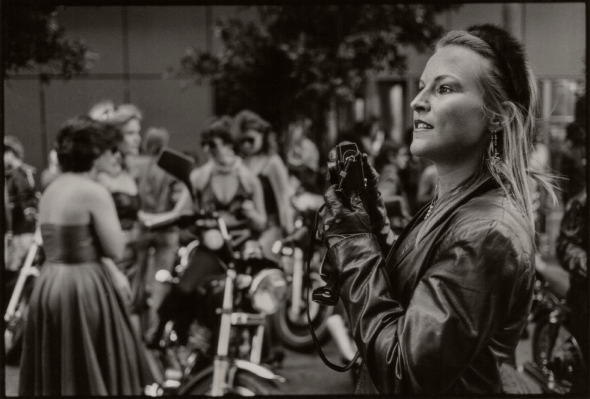 A thin blonde woman with long straight hair takes portraits of the Dykes on Bikes in a black and white photo.