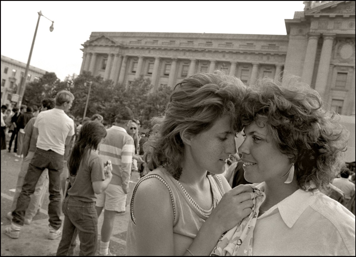 Portrait of a couple standing forehead to forehead outside the Civic Center in San Francisco. Both women are white with teased short hair.