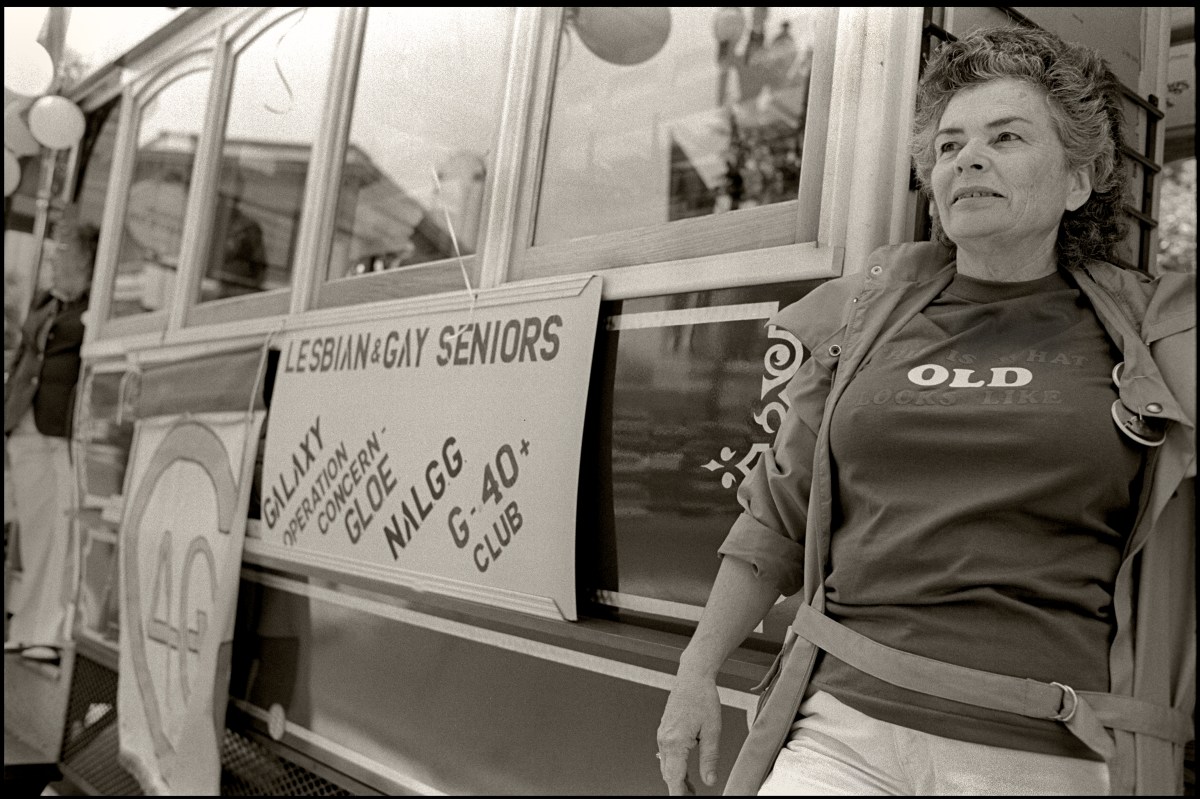 View of an unidentified woman, in a t-shirt that reads 'Old,' as she steps off a streetcar with a sign that reads, in part, 'Lesbian and Gay Seniors'.