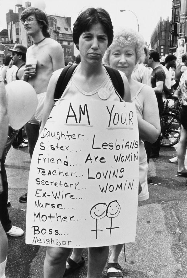 A lesbian has a sign that says I am your daughter, sister, friend, nurse, teacher, secretary, ex-wife, mother, a lesbian are women who love women