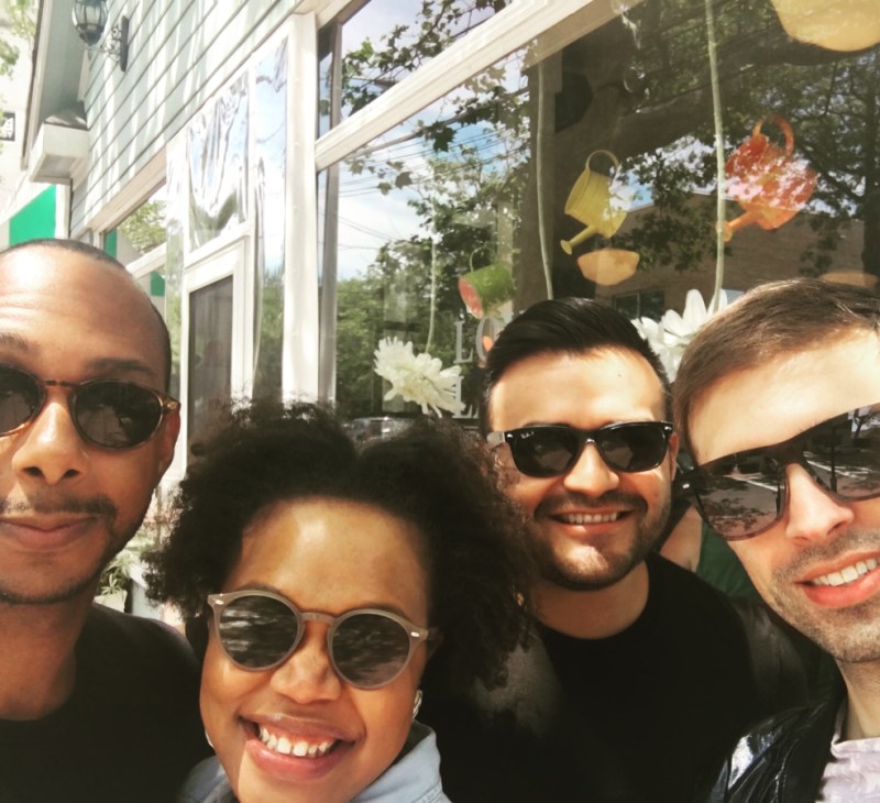 A photo of the author, who is a black woman in sunglasses with an afro in loose curls, with her friends on a summer day. There are three gay men, one is Black and the other two are Mexican, in the photo behind the author, all in sunglasses.