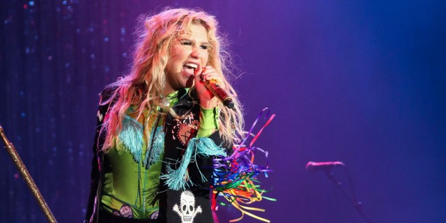 Kesha, who said "I'm not gay. I'm not straight." on Instagram yesterday, performs on stage in 2016. She is in a sparkling green bodysuit with long sleeves that have rainbow streamers coming off of the sides and a pirate symbol in front.
