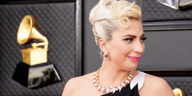 Lady Gaga is on the Grammys red carpet with her blonde hair pulled up into an updo with soft curls and one shoulder sleeveless black gown (we can only see her shoulders and above). She has pink lipstick.