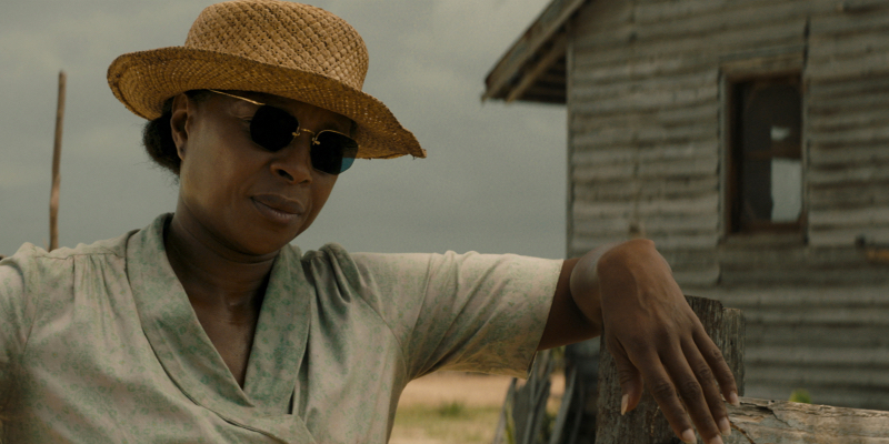 Mary J. Blige in a straw hat and sunglasses stands near a barn