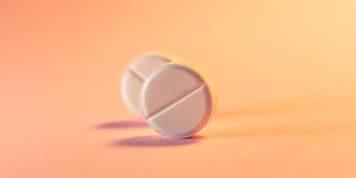 Two pills with diagonals across are rolling against an orange and pink background (the orange and pink lighting is also making the pills look pink)