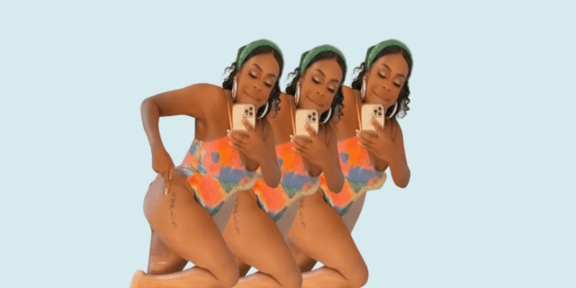 Niecy Nash wears a headband, hoop earrings, a one piece tie dye bathing suit, and points to her thigh tattoo.