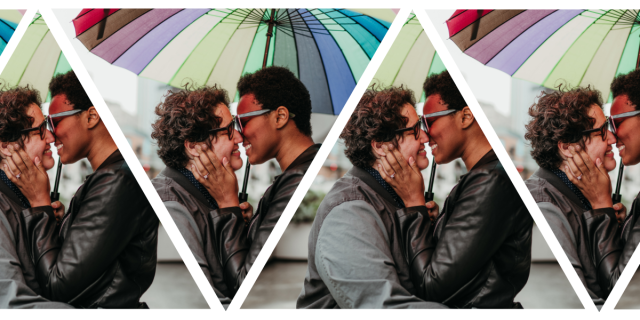Sa'iyda clasps her fiancee's face in her hands and looks at her lovingly. They stand beneath a rainbow umbrella. Sa'iyda is a Black woman who is wearing blue glasses and a leather jacket and has short hair. Beth, her fiancee, is a white woman with curly short brown hair and black glasses who is wearing a gray jean jacket. An engagement ring is conspicuously visibile on Sa'iyda's hand!