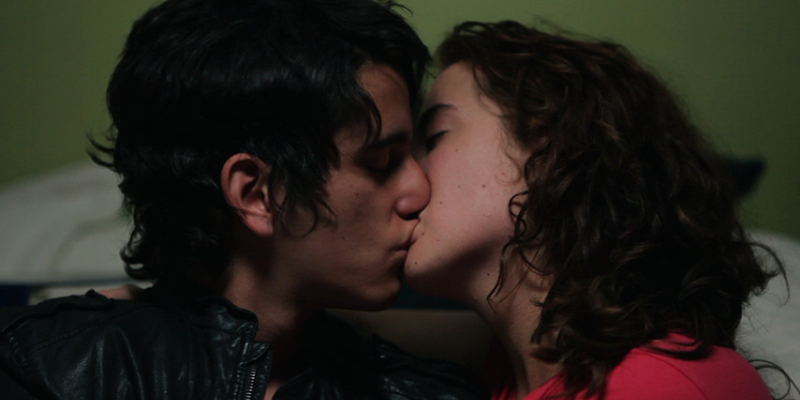 a close-up profile of a young man and young woman kissing both with shaggy brown hair.