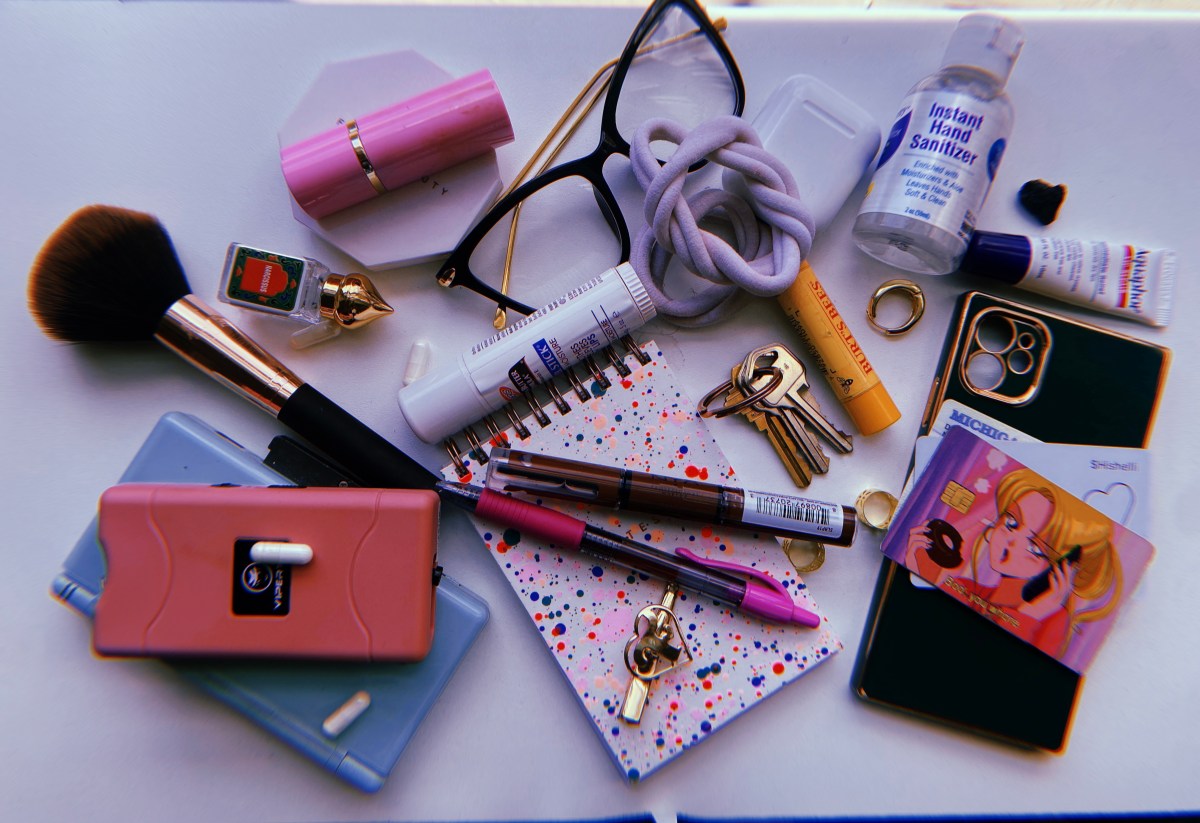 Shelli's things arranged artfully consist of a phone, wallet, notebook, cards withc ard covers, tazer, makeup brush, burt's bees, various small pieces of jewelry, lipstick, lip bams, hand snaitizer, hair bands, and non-prescription glasses