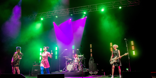Bikini Kill performs on stage with purple and green light