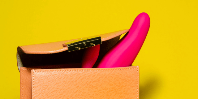 Against a yellow background, a light orange purse is slightly open, revealing two bright pink, silicone sex toys peeking out.