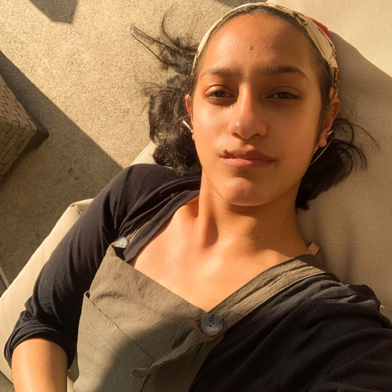 Lily is a Latine person laying on the ground with their hair flared around them like a halo