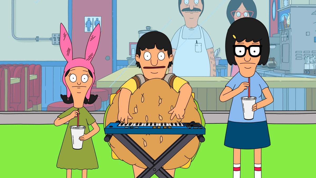 In a still from Bob's Burgers, Bob's three children are standing outside their father's burger joint. Left to right, there is Louise in a pink hat with bunny ears, then Gene in a burger suit playing piano, and Tina with a blue shirt and navy blue skirt, glasses, drinking a milkshake.