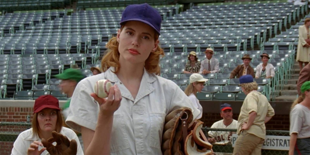 Geena Davis holds a baseball like "what?" while wearing a blue cap in A League of Their Own