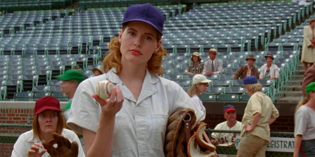 Geena Davis holds a baseball like "what?" while wearing a blue cap in A League of Their Own