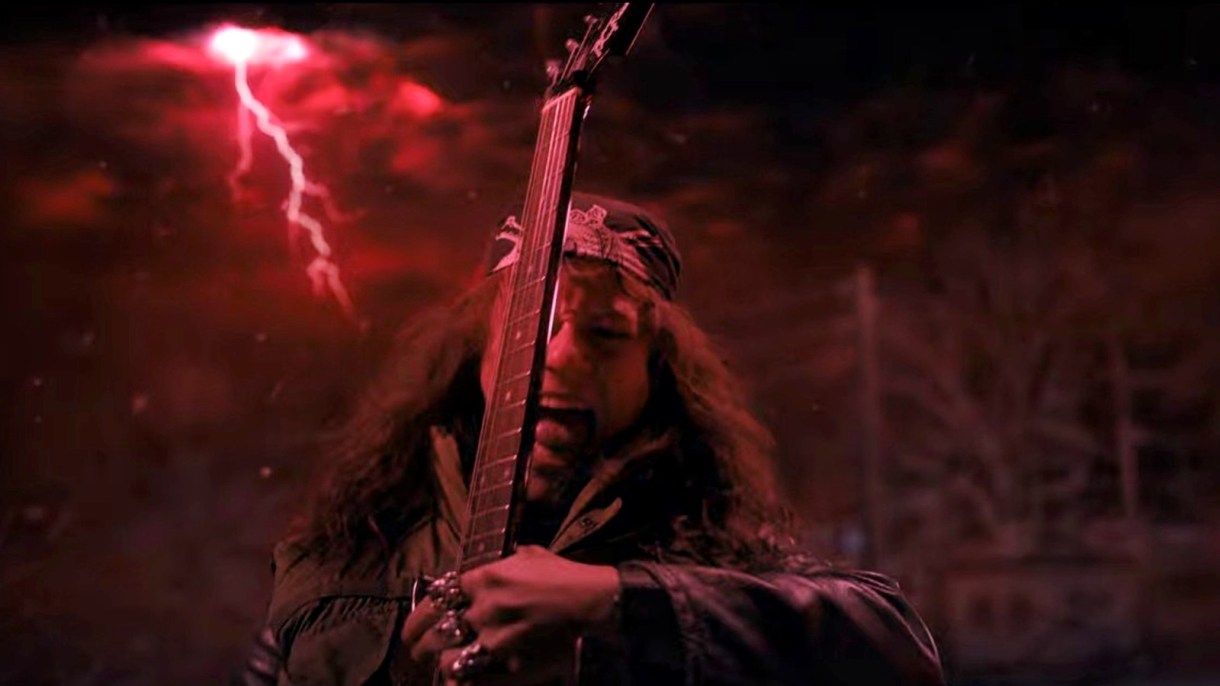 Eddie Munson tearing it up on an electric guitar in front of a spooky red background